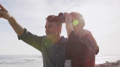 Caucasian-couple-enjoying-free-time-by-sea-on-sunny-day-holding-binoculars
