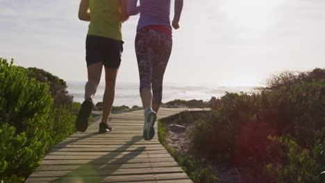 Caucasian-couple-enjoying-free-time-by-sea-on-sunny-day-running-path