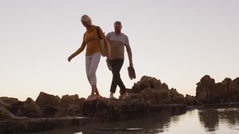 Senior-couple-walking-while-holding-hands-at-beach