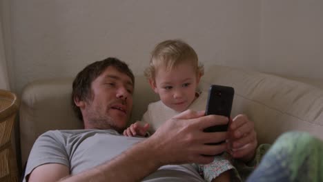 Caucasian-man-looking-smartphone-with-baby-at-home