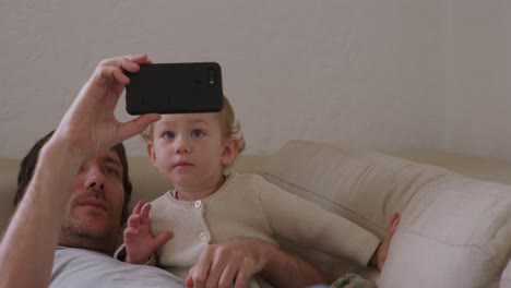 Hombre-Caucásico-Mirando-Smartphone-Con-Bebé-En-Casa