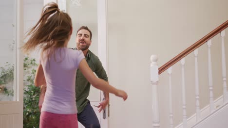 Caucasian-man-entering-the-front-door-of-his-house,-greeting-his-daughter
