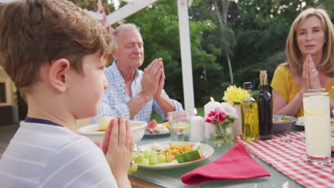 Three-generation-family-praying-before-having-lunch-outdoors