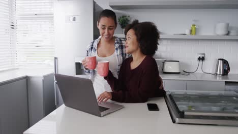 Lesbian-couple-having-coffee-and--using-laptop-in-kitchen