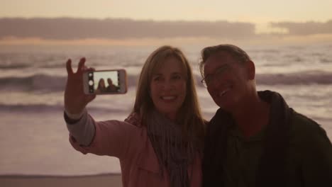 Active-senior-couple-taking-selfie-on-beach