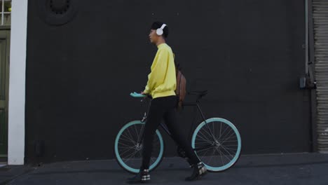 Transgender-adult-walking-with-a-bike-and-using-headphones