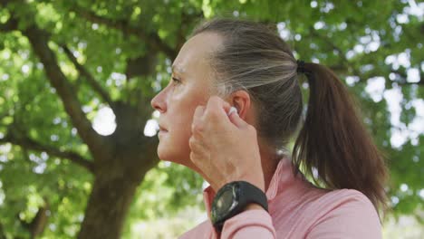 Senior-woman-using-wireless-earphones-in-the-park
