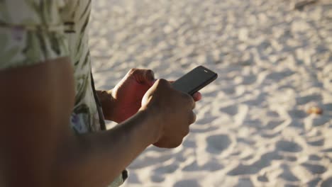 African-American-man-using-his-phone-at-beach-