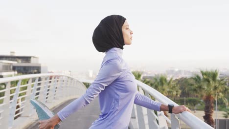 Side-view-of-woman-wearing-hijab-stretching-outside-looking-at-camera