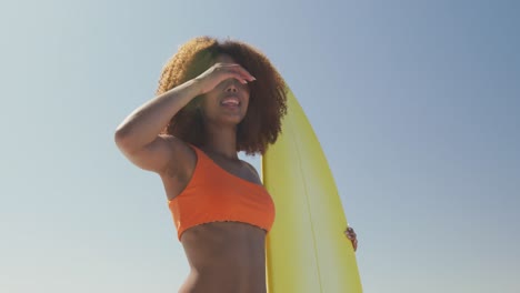 Mujer-Afroamericana-Mirando-La-Vista-Al-Mar-Con-Tabla-De-Surf