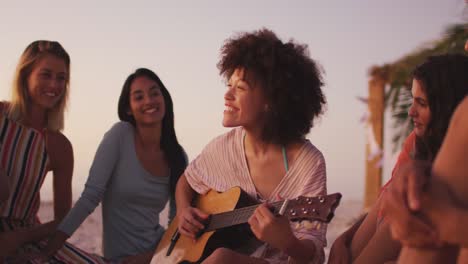 Frau-Mit-Gemischter-Abstammung,-Die-Am-Strand-Für-Ihre-Freunde-Gitarre-Spielt