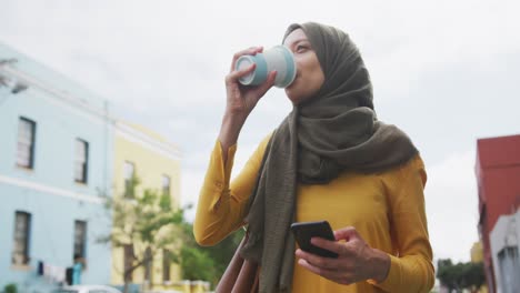 Mujer-Usando-Hijab-Usando-Un-Teléfono-Y-Tomando-Un-Café-Para-Llevar