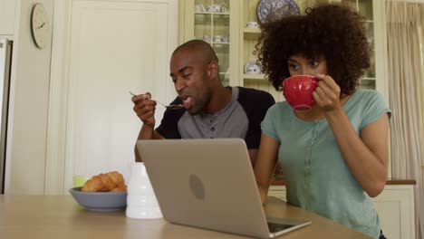 Happy-mixed-race-couple-eating-breakfast-in-their-kitchen