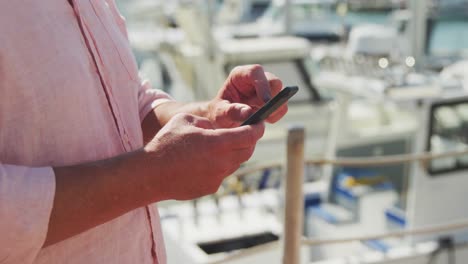 Side-view-mid-section-of-a-Caucasian-man-using-his-phone-harbor-side