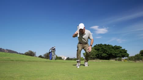 Caucasian-male-golfer-kneeling-on-a-golf-course-on-a-sunny-day