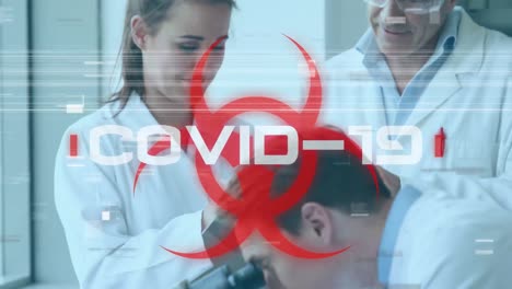 Das-Wort-„Covid-19“-Steht-Auf-Einem-Gesundheitsgefährdungsschild,-Im-Hintergrund-Arbeiten-Wissenschaftler
