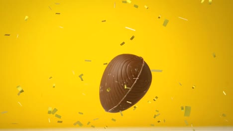 Animation-of-chocolate-Easter-egg-falling-and-golden-confetti-flying-on-yellow-background