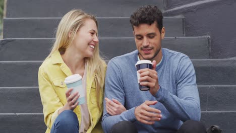 Front-view-of-Caucasian-couple-drinking-a-takeaway-coffee-sitting-on-stairs