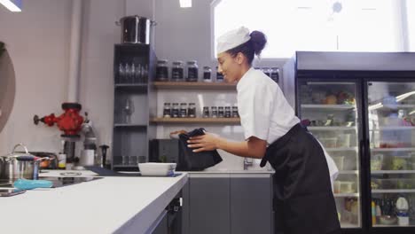 African-American-female-chef-wearing-chefs-whites-in-a-restaurant-kitchen,taking-food-out-of-an-oven