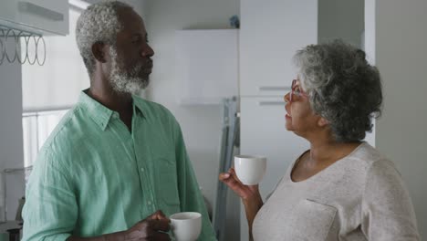 Ein-älteres-Afroamerikanisches-Paar-Zu-Hause,-Das-In-Sozialer-Distanzierung-Ein-Getränk-Trinkt