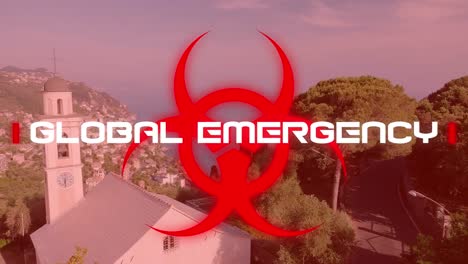 Animation-of-a-word-Global-Emergency-on-a-red-hazard-sign-over-a-drone-shot-of-fields-in-the-backgro