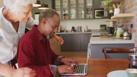 Senior-African-American-husband-and-mixed-race-wife-happily-working-on-a-laptop-at-home