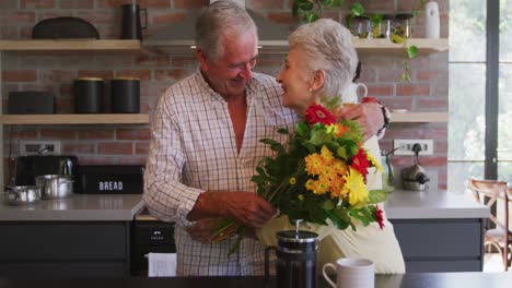 Senior-Caucasian-husband-offering-flowers-to-his-wife,-hugging-and-smiling