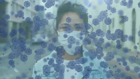 Animation-of-macro-Covid-19-cells-floating-over-Asian-woman-wearing-a-face-mask-Outside-