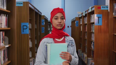 Porträt-Einer-Lächelnden-Asiatischen-Studentin,-Die-Einen-Roten-Hijab-Trägt-Und-In-Einer-Bibliothek-Studiert