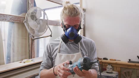 Caucasian-male-surfboard-maker-wearing-a-face-mask-and-making-a-surfboard