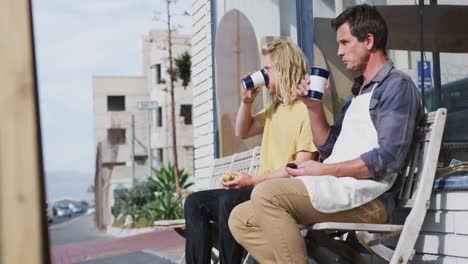Two-Caucasian-male-surfboard-makers-sitting-on-a-bench-and-drinking-takeaway-coffee