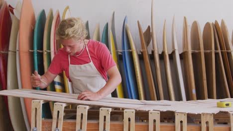 Caucasian-male-surfboard-maker-working-in-his-studio-and-making-a-wooden-surfboard