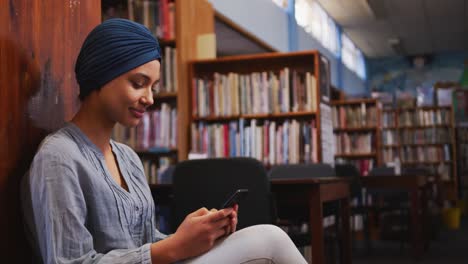 A-happy-Asian-female-student-wearing-a-blue-hijab-sitting-and-using-a-smartphone