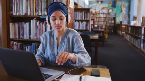 Estudiante-Asiática-Con-Un-Hijab-Azul-Sentada-Y-Usando-Una-Computadora-Portátil-En-La-Biblioteca