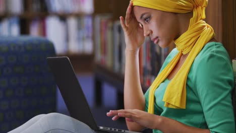 Asian-female-student-wearing-a-yellow-hijab-sitting-and-using-laptop