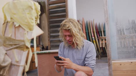 Caucasian-male-surfboard-maker-taking-a-photo-of-a-wooden-surfboard-with-his-smartphone