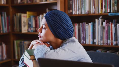 Asian-female-student-wearing-a-blue-hijab-sitting-and-leaning-on-a-pile-of-books-and-thinking