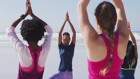 Multi-ethnic-group-of-women-doing-yoga-position-on-the-beach-and-blue-sky-background