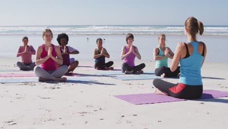 Multiethnische-Gruppe-Von-Frauen,-Die-Yoga-Machen-Und-Hände-Am-Strand-Und-Im-Hintergrund-Des-Blauen-Himmels-Sammeln