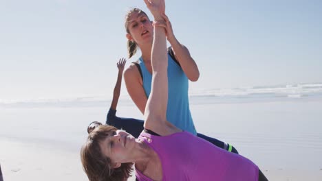 Caucasian-yoga-teacher-woman-helping-woman-on-the-beach-and-blue-sky-background