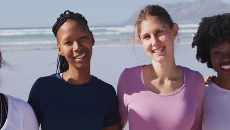 Multiethnische-Gruppe-Von-Frauen,-Die-In-Die-Kamera-Schauen-Und-Am-Strand-Und-Vor-Blauem-Himmel-Lächeln