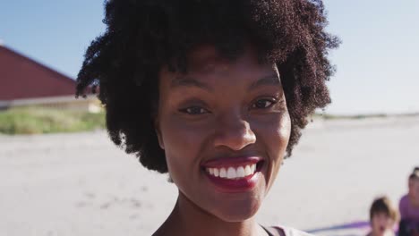 Mujer-Afroamericana-Mirando-La-Cámara-Y-Sonriendo-En-La-Playa-Y-El-Fondo-Del-Cielo-Azul