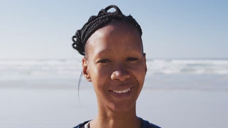 Mujer-Afroamericana-Mirando-La-Cámara-Y-Sonriendo-En-La-Playa-Y-El-Fondo-Del-Cielo-Azul