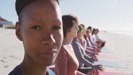 Multiethnische-Gruppe-Von-Frauen,-Die-Yoga-Position-Machen,-Und-Afroamerikanerin,-Die-Am-Strand-In-Die-Kamera-Schaut