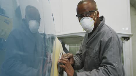 Afroamerikanischer-Männlicher-Automechaniker,-Der-Eine-Gesichtsmaske-Trägt-Und-Einen-Polierer-An-Der-Seite-Eines-Autos-Benutzt