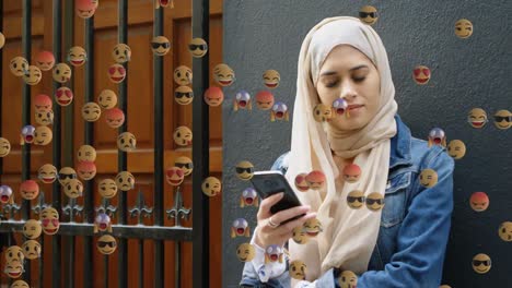 Face-emojis-moving-against-woman-in-hijab-using-smartphone