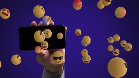 Hand-holding-smartphone-with-emoticons-spawning