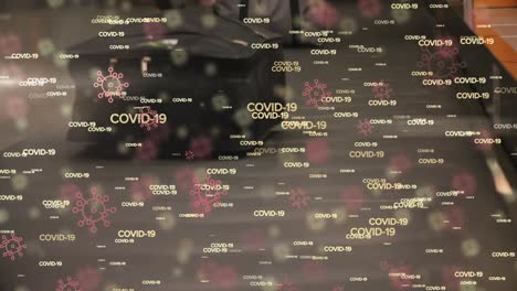 Digital-composite-video-of-Covid-19-cells-text-and-icons-against-luggage-conveyor-belt-in-background
