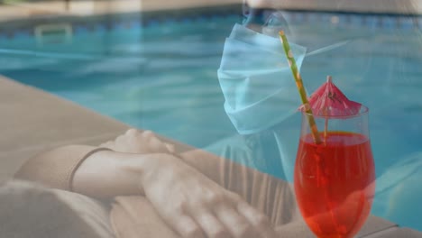 Digital-composite-video-of-glass-of-drink-by-the-pool-against-woman-wearing-face-mask-in-background