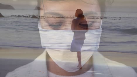Digital-composite-video-of-woman-wearing-a-face-mask-against-woman-walking-on-the-beach